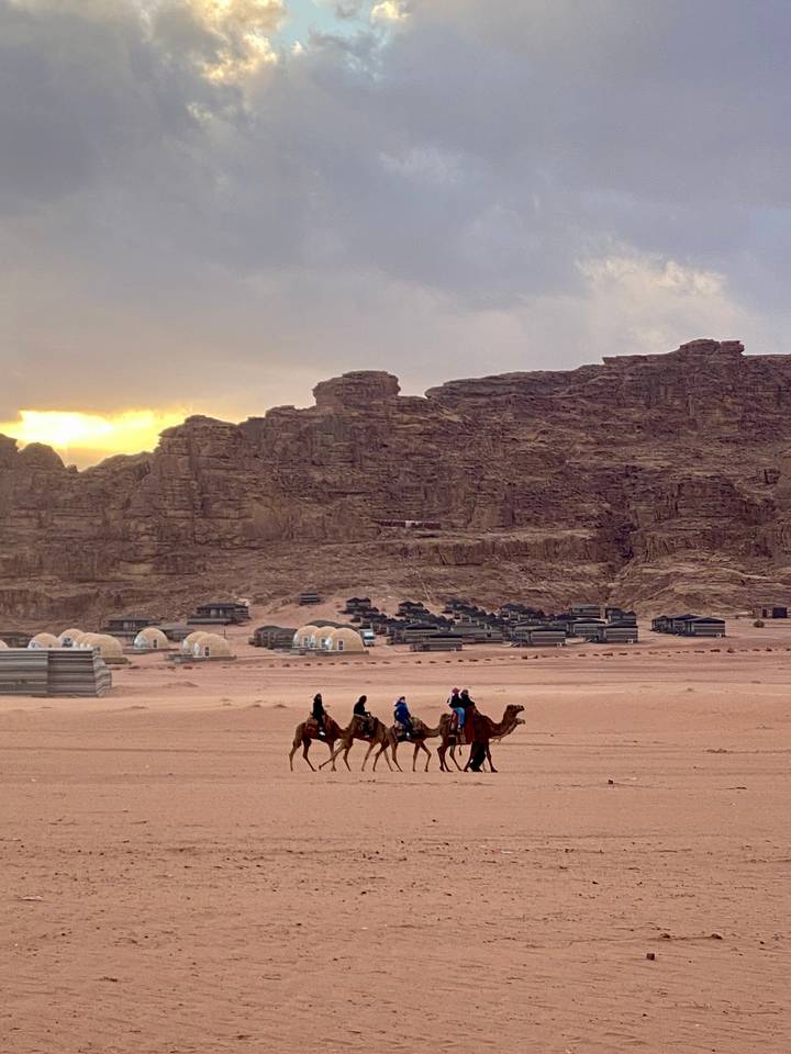 Des gens chevauchant des chameaux dans un paysage désertique avec des tentes.