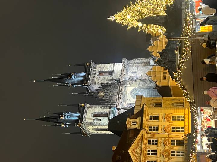 Iglesia histórica con torres iluminadas por la noche con gente en primer plano.