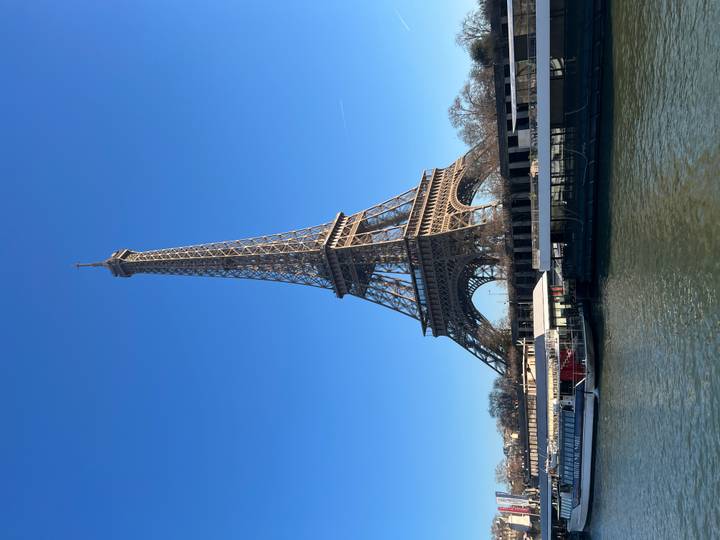 Torre Eiffel con cielo despejado sobre el río con barcos.
