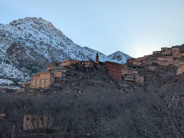 Maisons de village sur un flanc de montagne avec des sommets enneigés.
