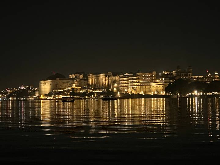 Palace complex lit up at night, reflecting on water.