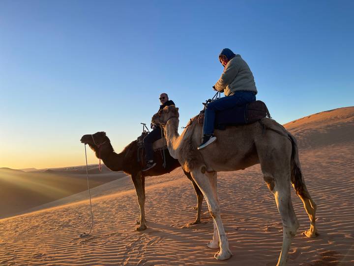Deux personnes à dos de chameaux dans le désert au coucher du soleil.