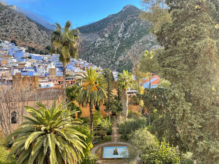 Vue de Chefchaouen avec des jardins luxuriants et des montagnes en arrière-plan.