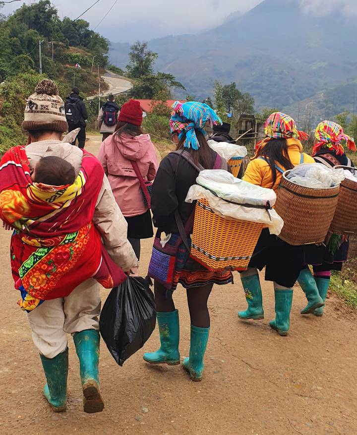 Grupo de personas caminando por un sendero de tierra, cargando cestas coloridas.