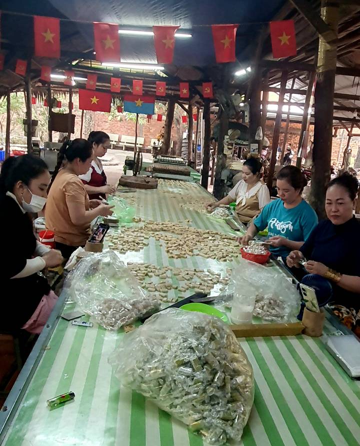 Mujeres trabajando en una mesa con varios materiales en un entorno de fábrica.