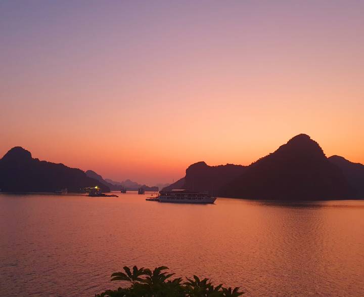 Vista del atardecer sobre la Bahía de Halong con barcos y montañas kársticas.