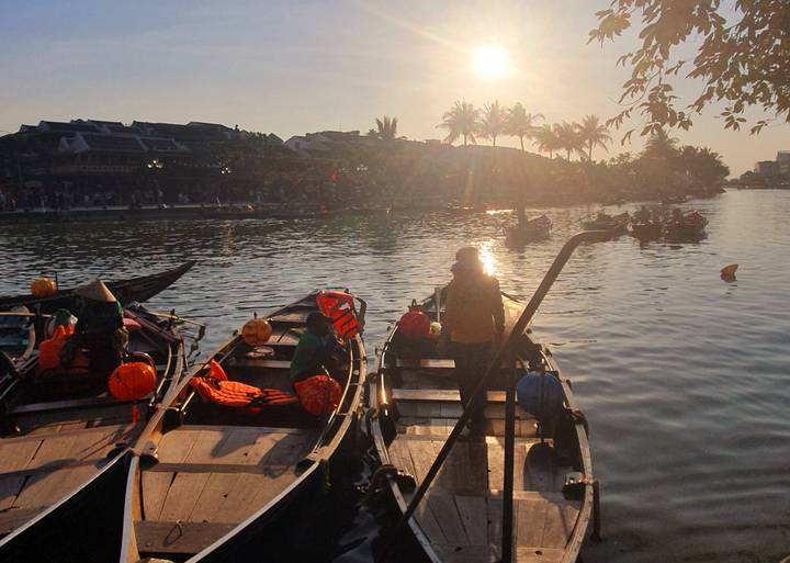 Barcos en un río al atardecer, con gente y faroles.