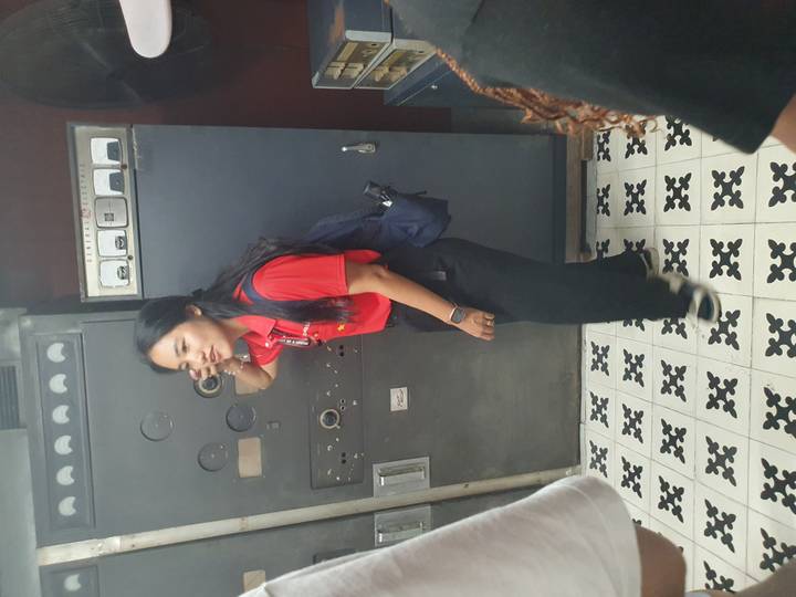 Mujer de pie en un interior con equipo industrial.