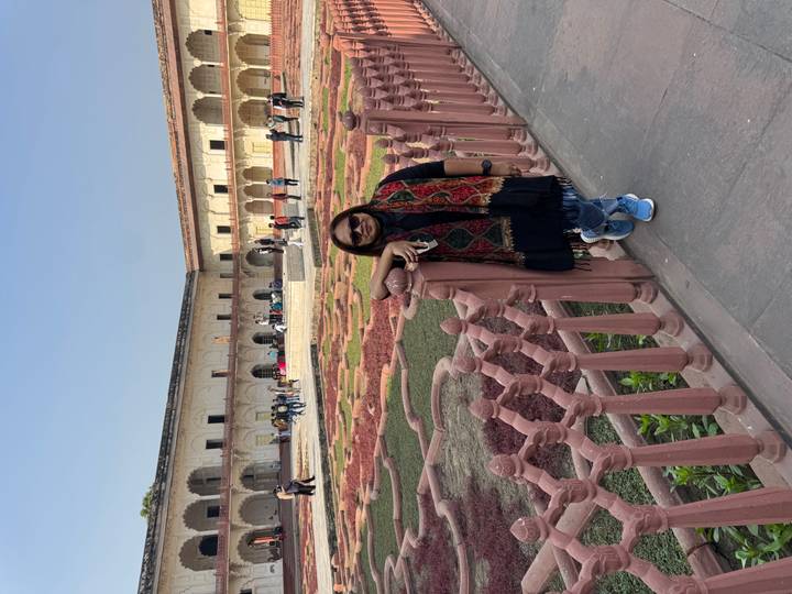 Mujer apoyada contra una cerca dentro de un jardín ornamentado.