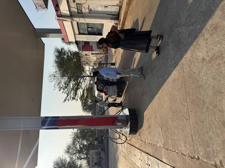 Personas en una gasolinera, con autos estacionados bajo el toldo.