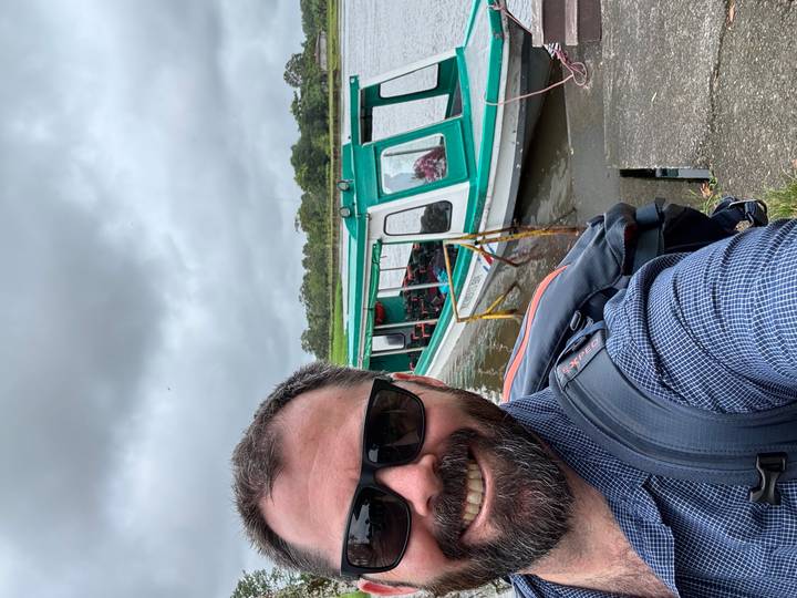 Selfie d'une personne avec des lunettes de soleil près d'un bateau sur une rivière.