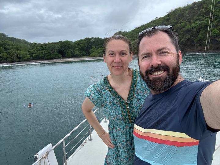 Couple prenant un selfie sur un bateau avec une plage en arrière-plan.