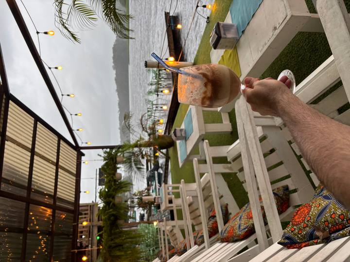 Main tenant un verre de boisson sur une terrasse au bord du lac.