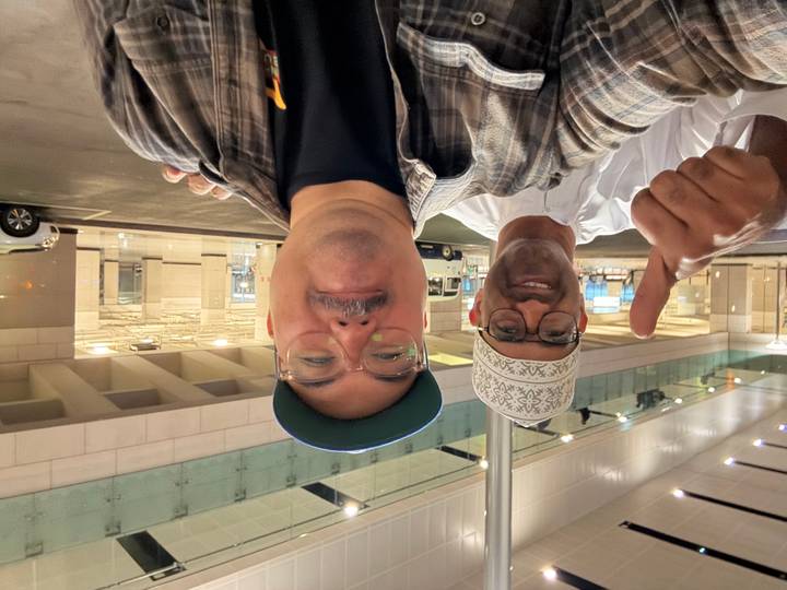 Dos personas posando para una foto, una haciendo el gesto de pulgar hacia arriba.