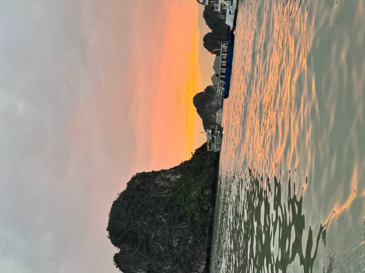 Vue du coucher de soleil sur la baie d'Halong avec bateaux et falaises calcaires.