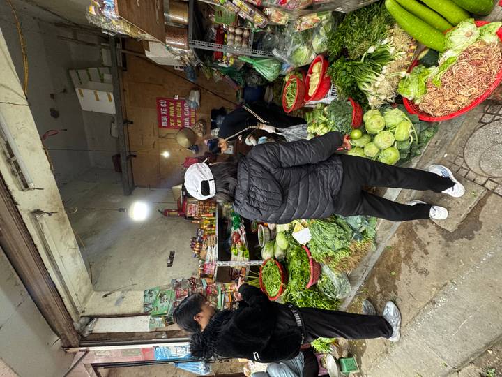 Personas comprando en un puesto de verduras en un mercado cubierto.