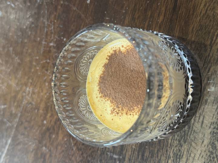 Copa de vidrio llena de un postre cremoso cubierto con cacao en polvo.