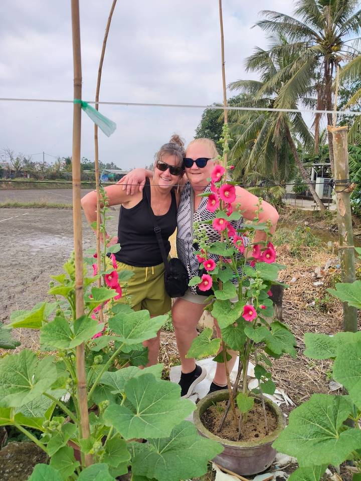 Deux femmes souriantes avec un jardin de fleurs au premier plan.