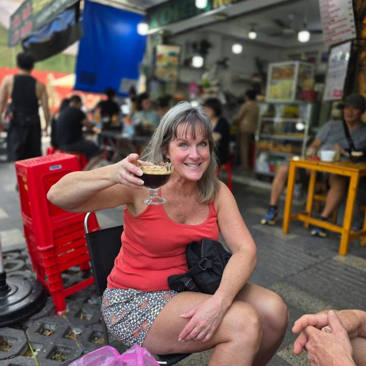 Femme tenant un verre de boisson foncée avec un arrière-plan de marché.