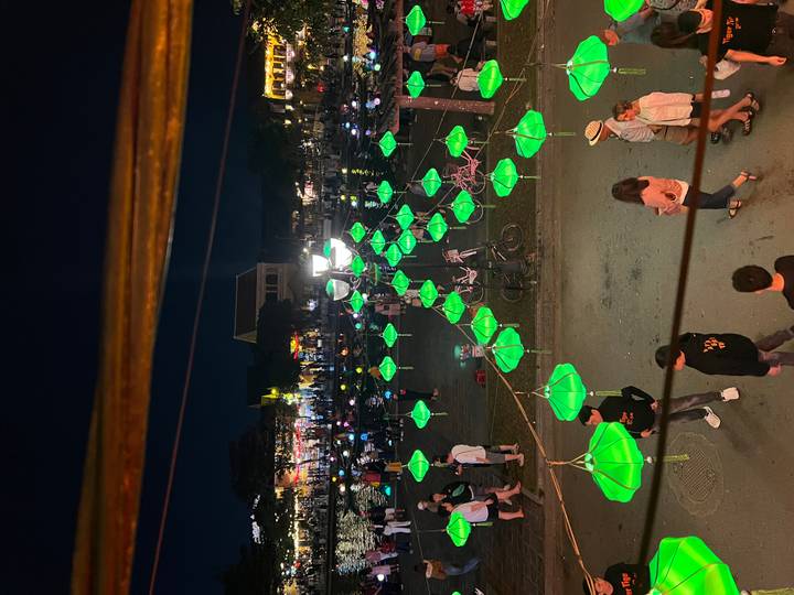 Des lanternes vertes vives menant le long d'un sentier avec de l'eau et des gens visibles en contrebas.