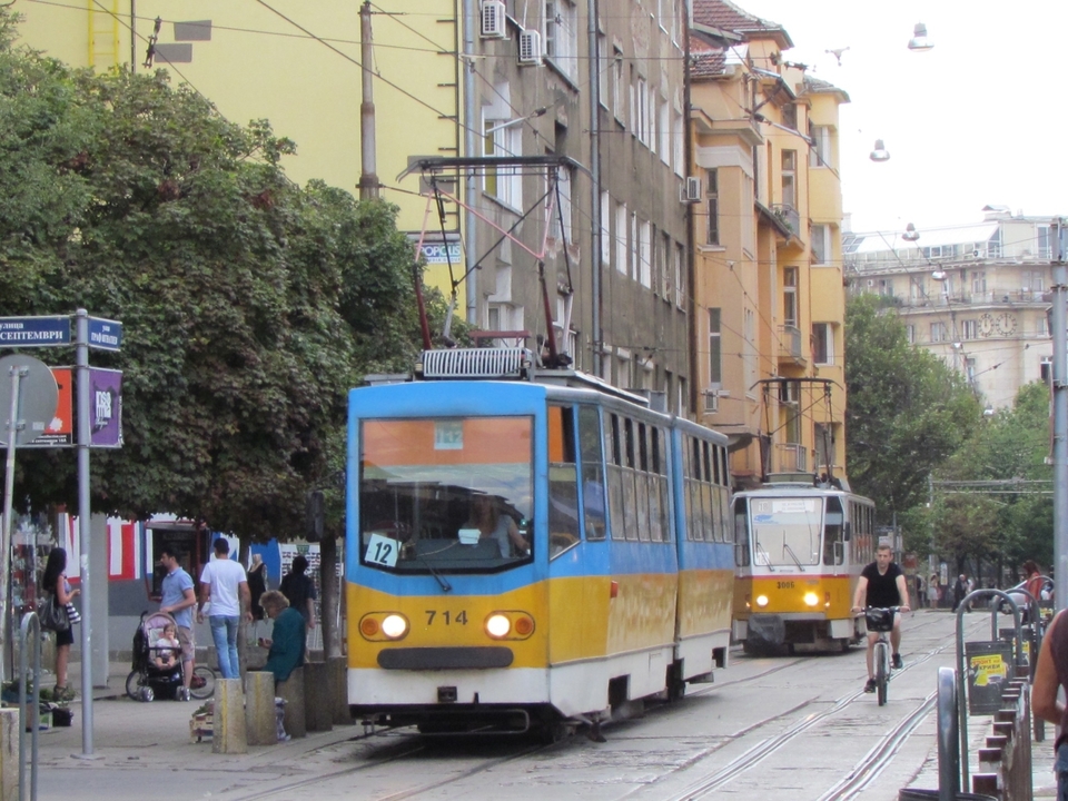 Trams on a street with people walking along the roadside.