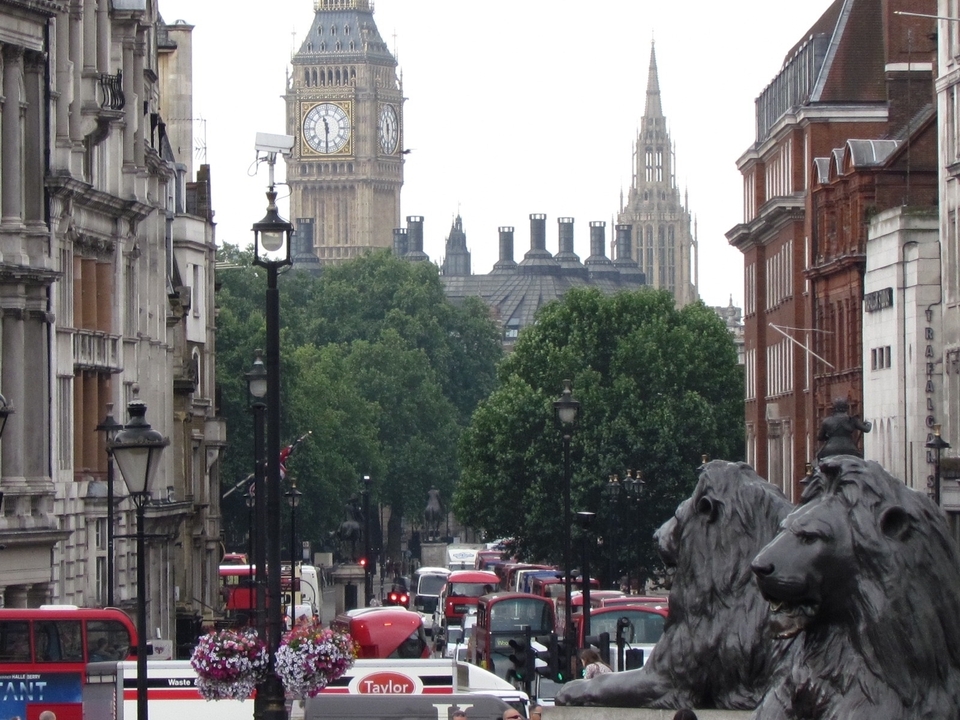 Busy street with red buses, clock tower, and historic buildings.
