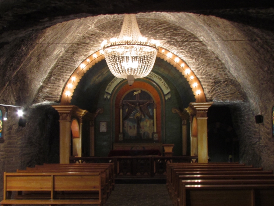An underground chapel with a chandelier and wooden pews.