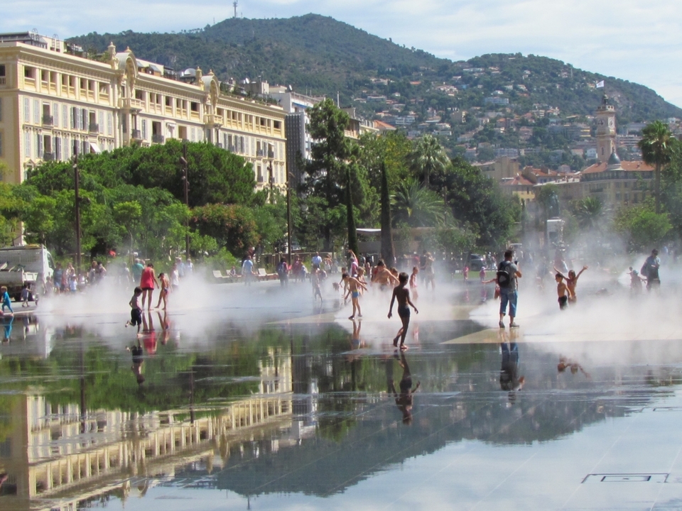 People playing in mist at a public park with fountains.