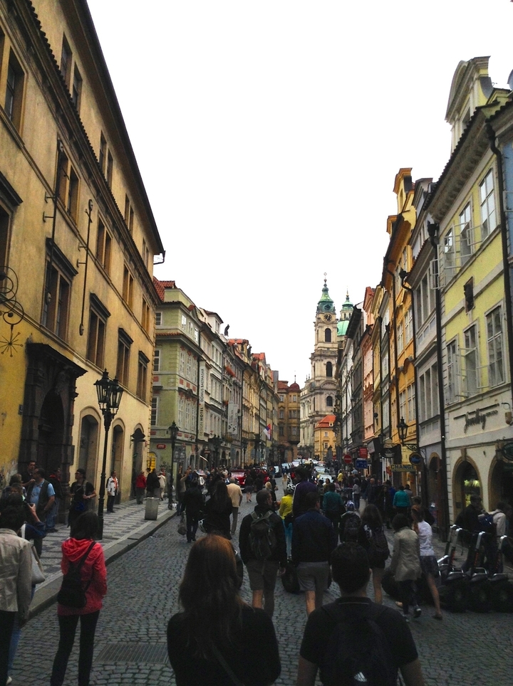 A street view with ornate buildings, leading to a church with a green dome.