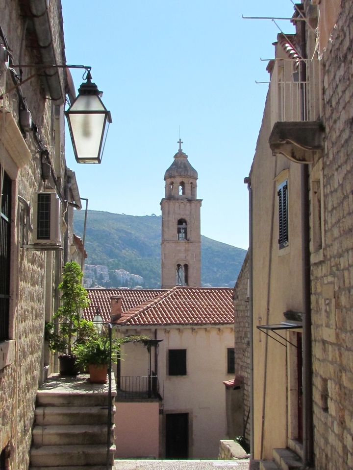 A scenic view of a historical clock tower in a city with terracotta rooftops and hills in the background.