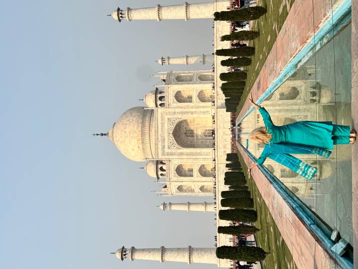 Une personne les bras ouverts face au Taj Mahal avec son reflet sur l'eau.