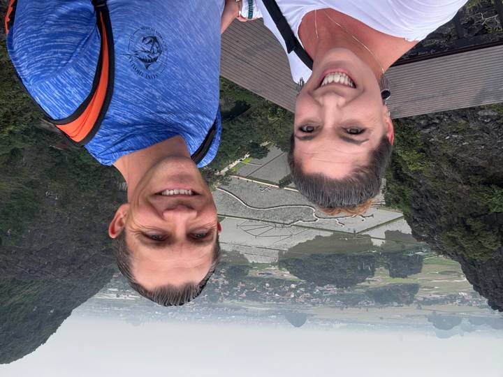 Un couple prenant un selfie avec une vue panoramique sur des rizières en terrasses et des montagnes calcaires en arrière-plan.