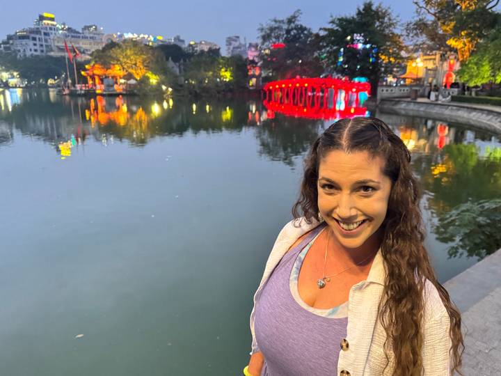 Une femme debout près d'un plan d'eau avec des lumières de pont rouge vif reflétées sur l'eau.