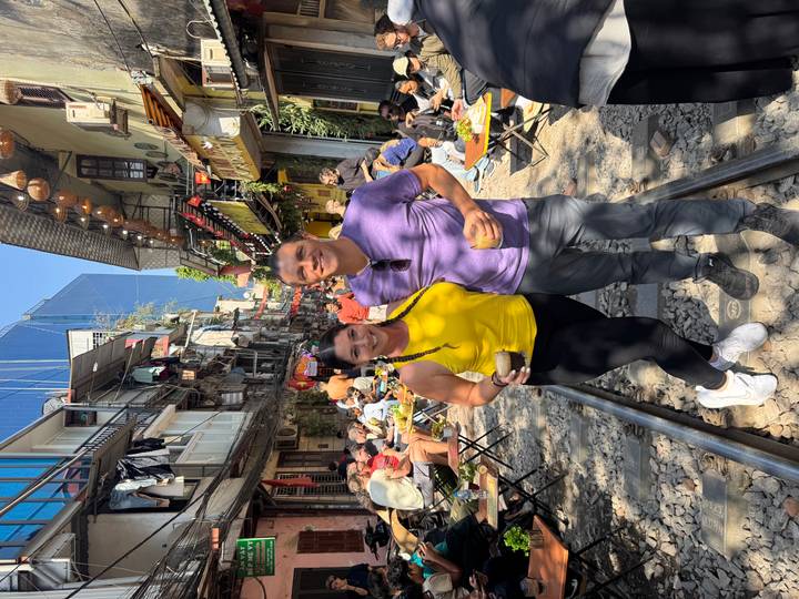 Un couple debout sur des rails de chemin de fer dans une rue bondée avec des gens qui dînent dehors.