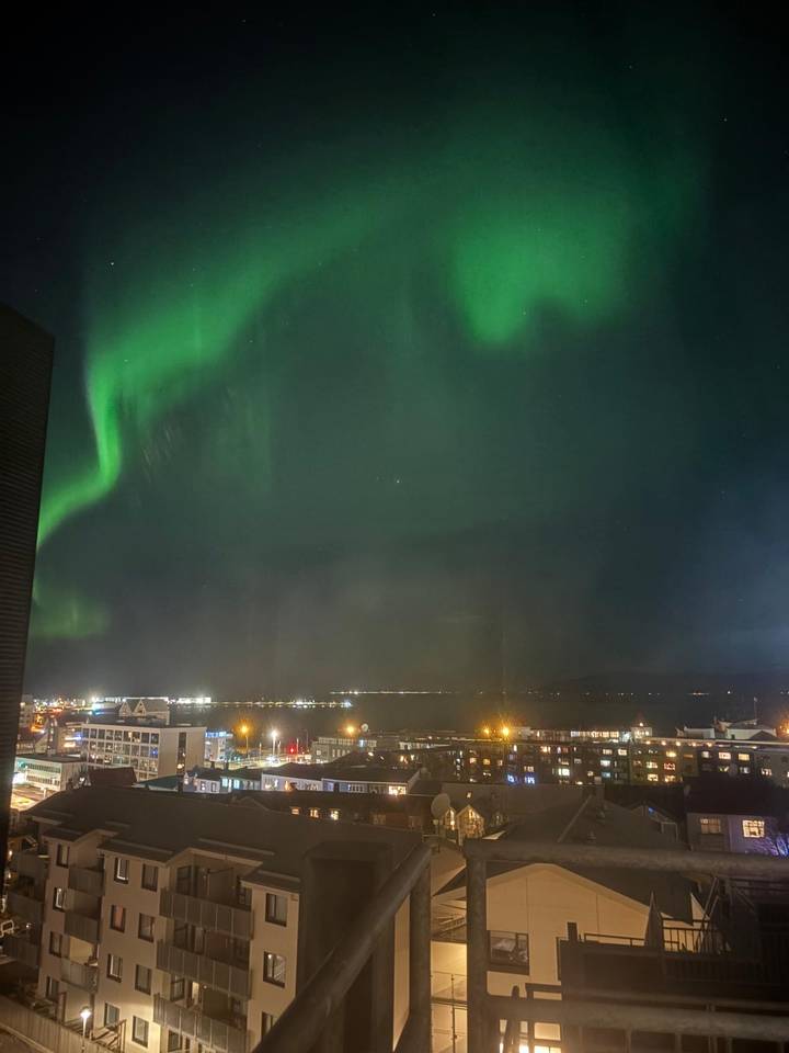 Vue des lumières de la ville sous une aurore boréale verte éclatante.