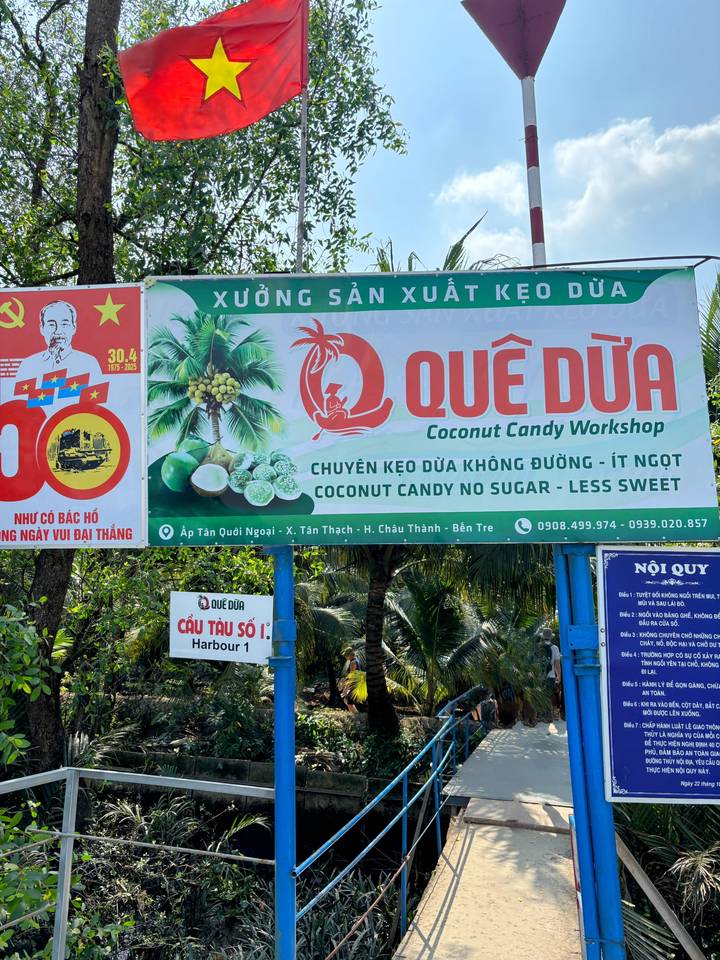 Letrero del Taller de Dulces de Coco Quê Dừa rodeado de palmeras.