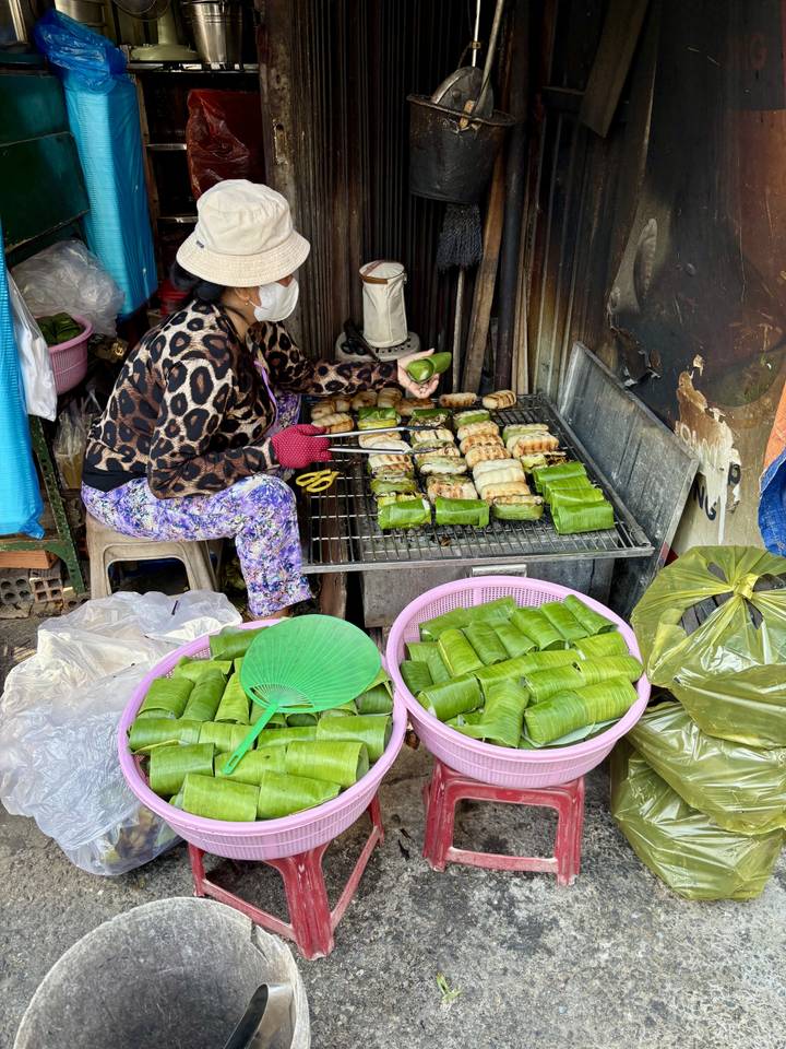 Vendedor preparando comida envuelta en hojas de plátano en un mercado callejero.