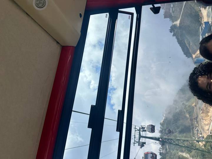 Dentro de un teleférico con una persona parcialmente visible y montañas pintorescas afuera.