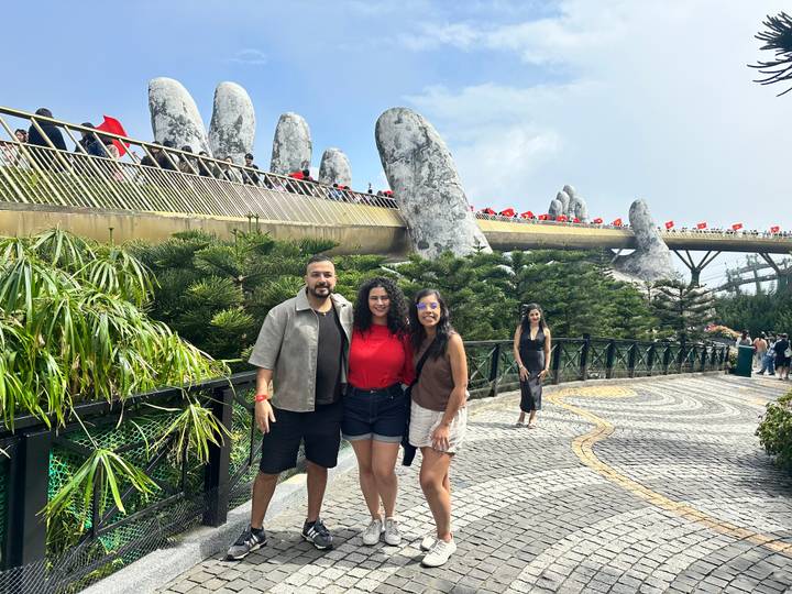 Tres personas paradas frente al famoso Puente Dorado con esculturas de manos.
