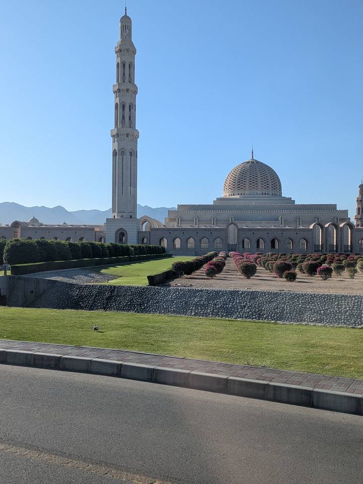 Gran mezquita con diseños intrincados rodeada de jardines y montañas al fondo.