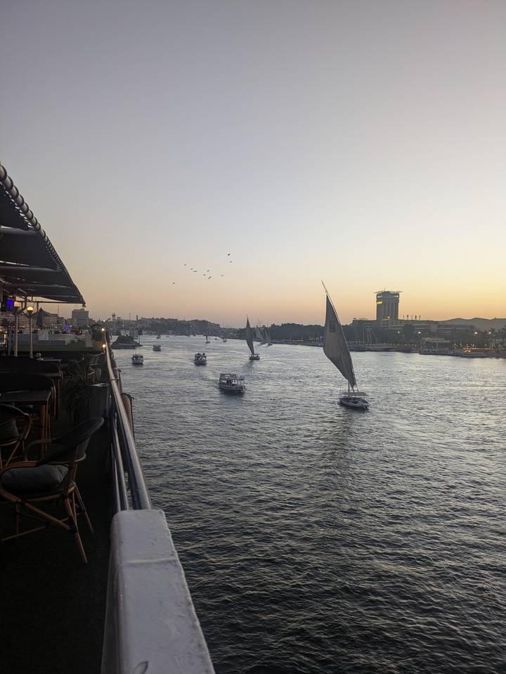Atardecer sobre un río con veleros y el horizonte de la ciudad.