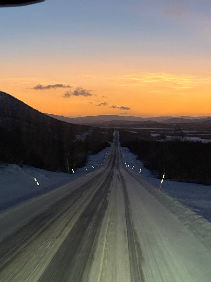 Snowy road leading into a sunset with mountains in the distance.