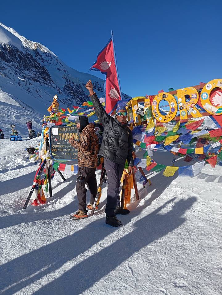 Dos personas posando with banderas de oración en un paso de montaña cubierto de nieve.