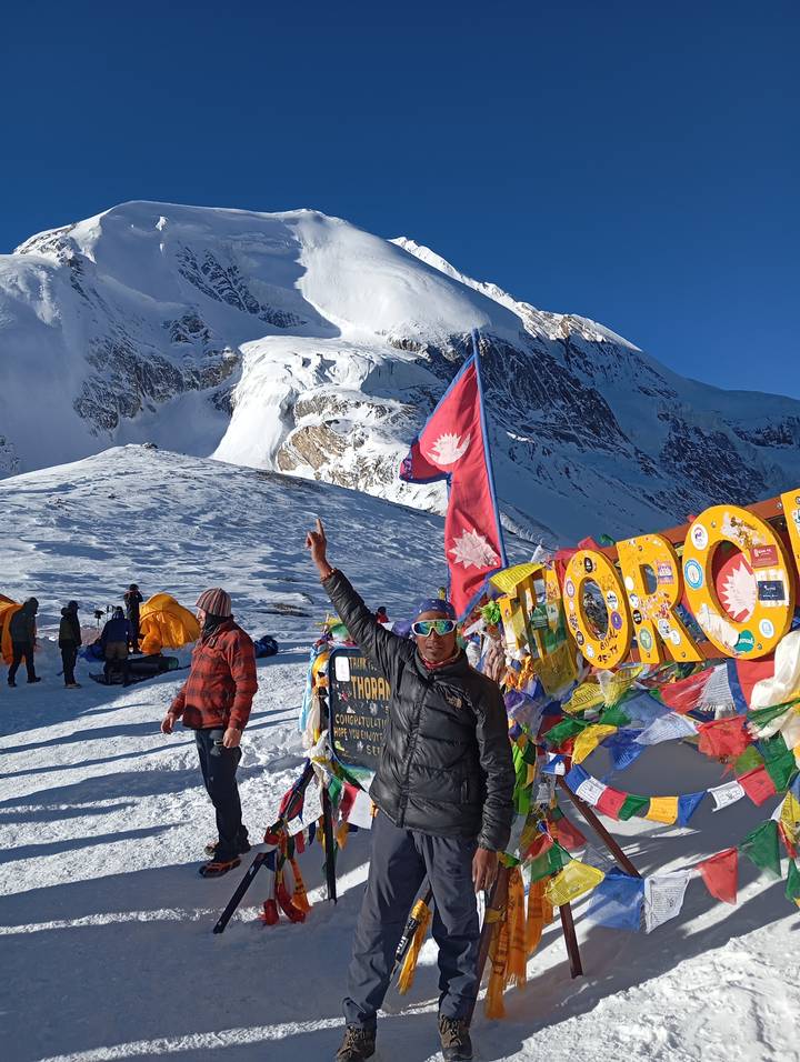 Una persona de pie frente a banderas de oración con una montaña cubierta de nieve al fondo.