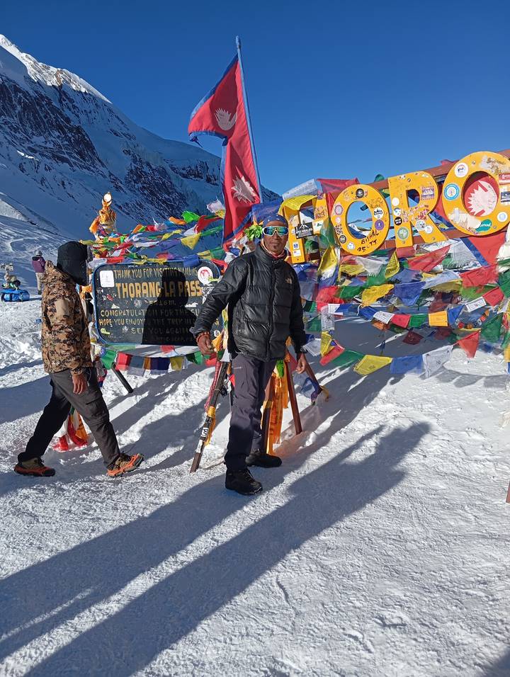 Dos personas celebrando en un paso de montaña nevado con banderas coloridas.