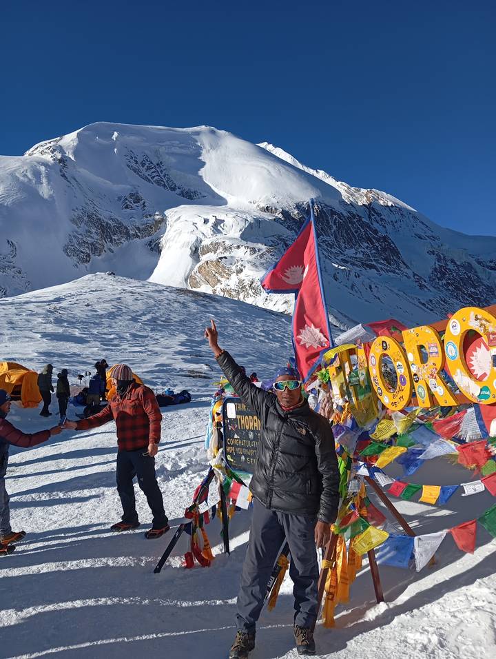 Una persona posando en un paso de montaña nevado con banderas coloridas.