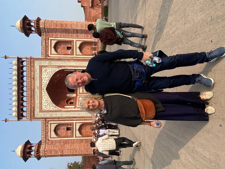 Couple posing in front of a red and white building with intricate designs.