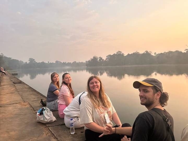 Un grupo de personas sentadas junto a un río tranquilo durante la puesta de sol.
