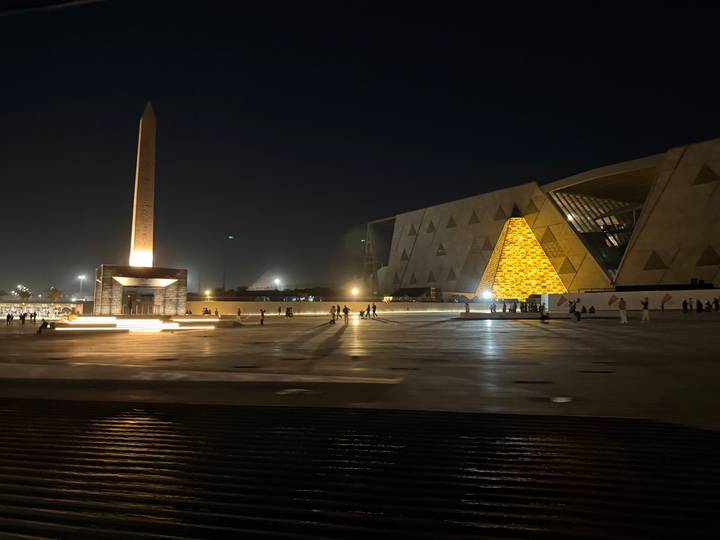 Gran estructura moderna con un obelisco, iluminada durante la noche.