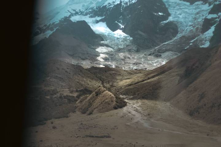 A mountainous landscape with patches of snow under cloudy skies.